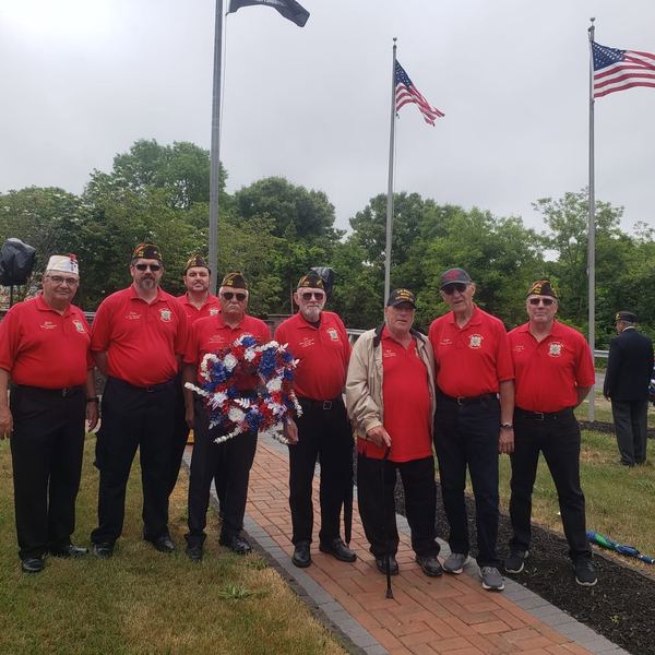 Post 400 members in red shirts standing with a wreath beside flagpoles